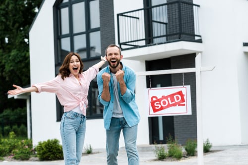 cheerful man and woman celebrating about purchasing a new investment property in front of board with sold letters